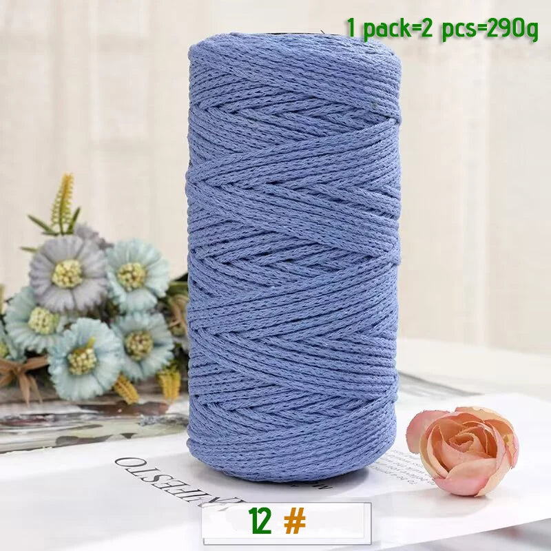 A spool of medium-thick blue yarn used for crafting, next to a pink rose and greenery.