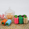A collection of spools of various colored sewing threads on a woven mat.
