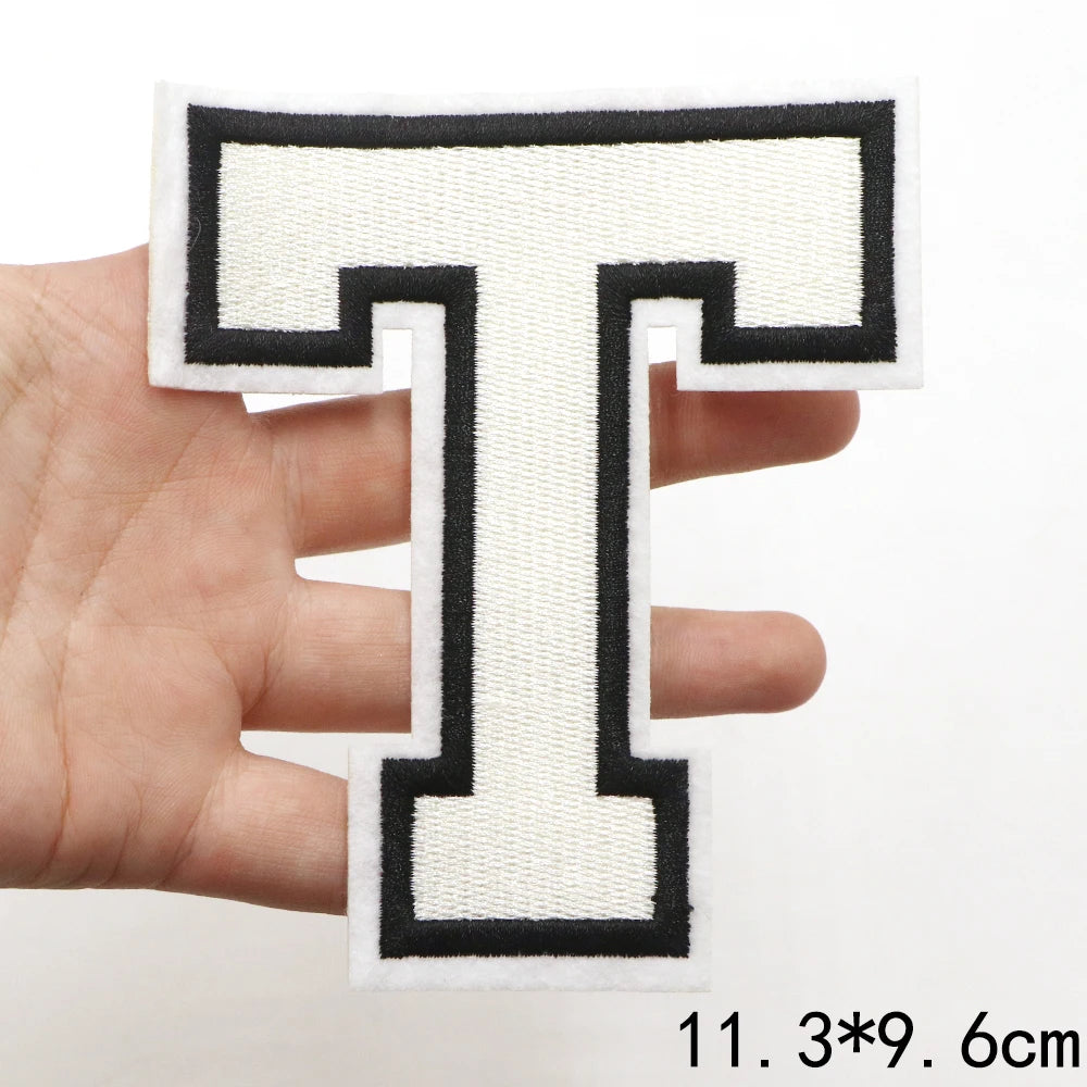 A hand holds a white and black letter T patch for clothing decoration.