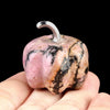 A handcrafted natural stone pumpkin figurine with pink and black marbled patterns is held in a hand.