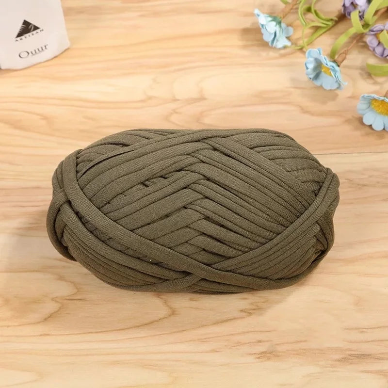 A ball of olive green flat thread yarn for crafting and sewing resting on a wooden surface.