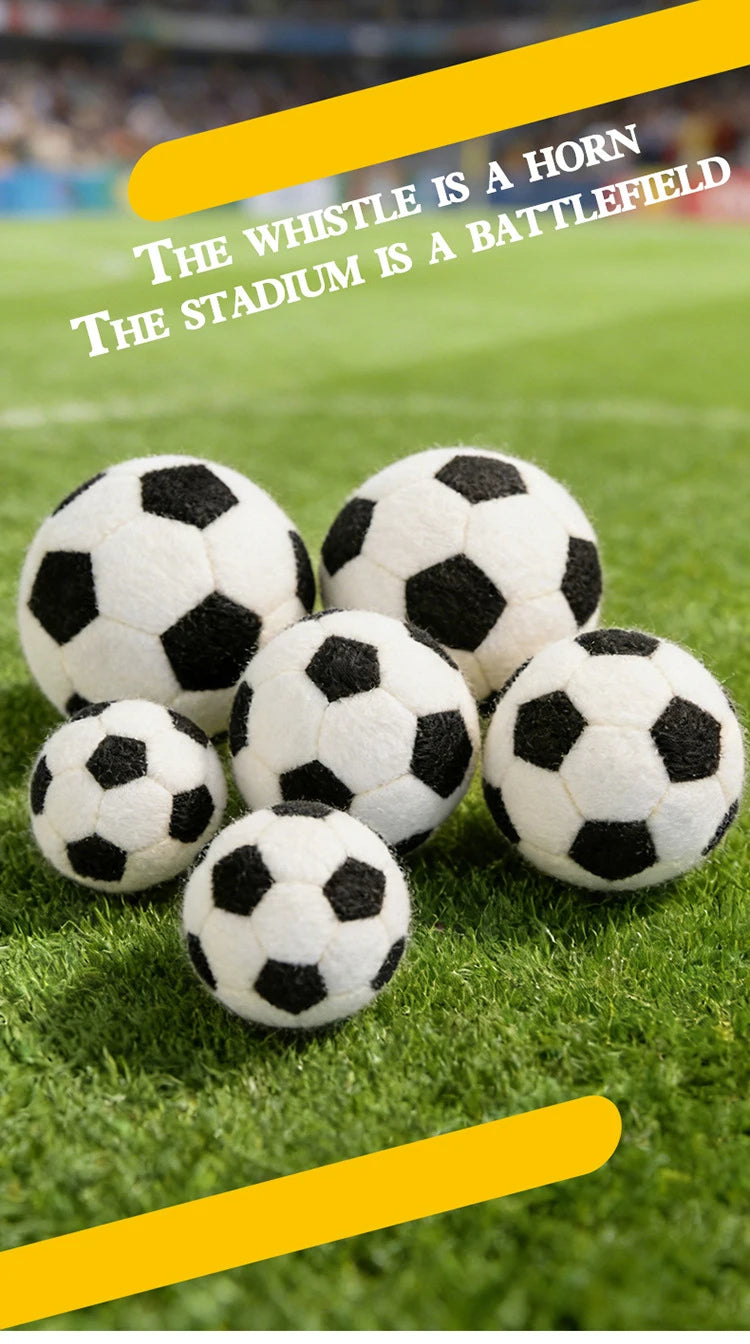 A close-up of several black and white football plush toys resting on green grass with a yellow text overlay.