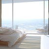 A bright bedroom interior featuring a bed with white linens and large glass doors overlooking a vast landscape.