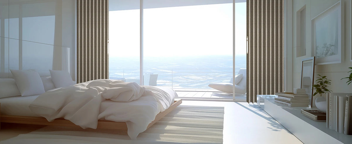 A bright bedroom interior featuring a bed with white linens and large glass doors overlooking a vast landscape.