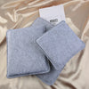 A stack of gray needle felting mat pads resting on a satin fabric with a white card.