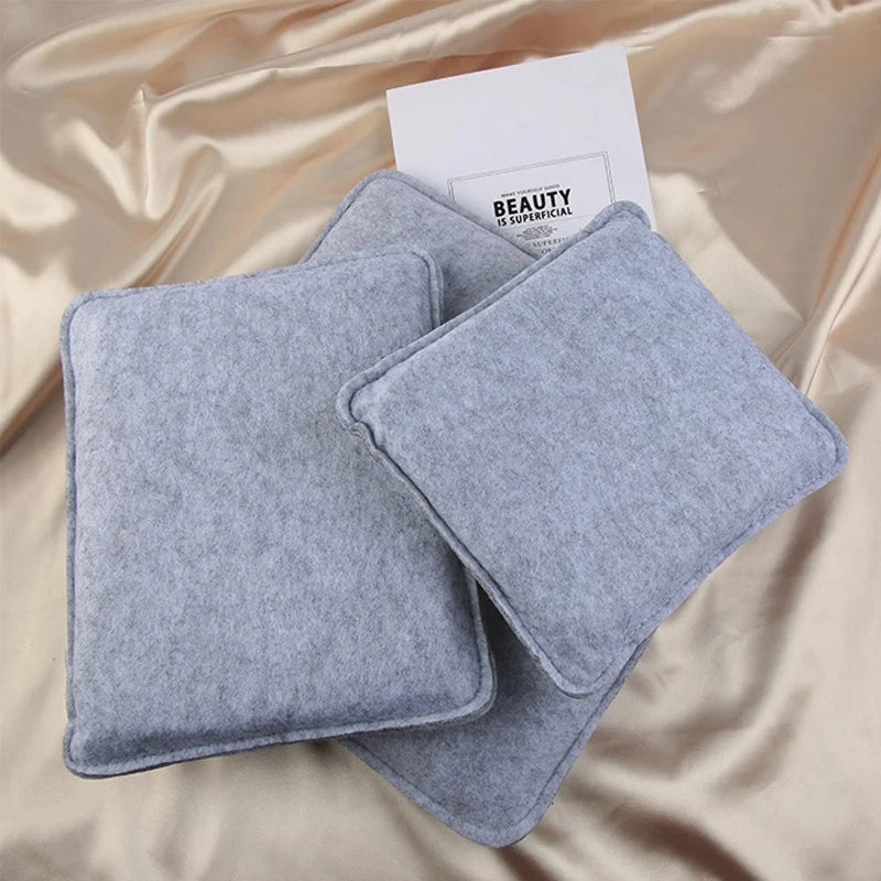 A stack of gray needle felting mat pads resting on a satin fabric with a white card.