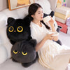 A woman is relaxing while holding a cup, with two black cat plush toys resting on the white sofa.