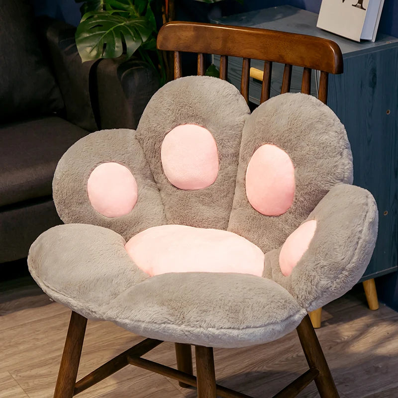 A soft gray plush bear paw cushion resting on a wooden chair.