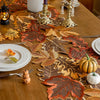 A rustic farmhouse maple leaf table runner featuring autumn-toned leaves in brown, orange, and gold on a wooden table.