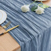 Blue linen table runner with white roses and gold cutlery on a wooden table.