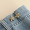 A close-up of blue denim fabric with two gold star-shaped button clips used for waist tightening.