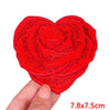 A bright red heart-shaped rose embroidery patch is held by a hand, showing its texture and size.