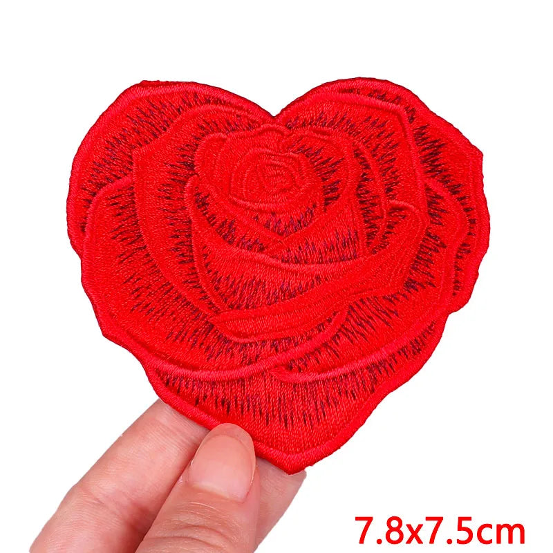 A bright red heart-shaped rose embroidery patch is held by a hand, showing its texture and size.