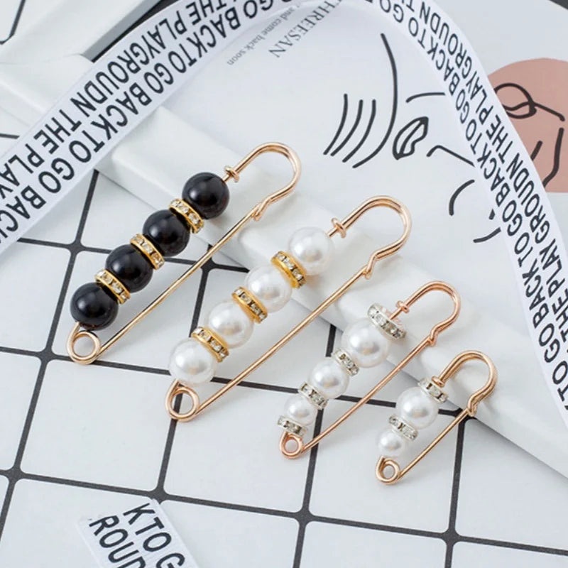 Gold-toned adjustable pearl brooches displayed on a white background with a spiral notebook.