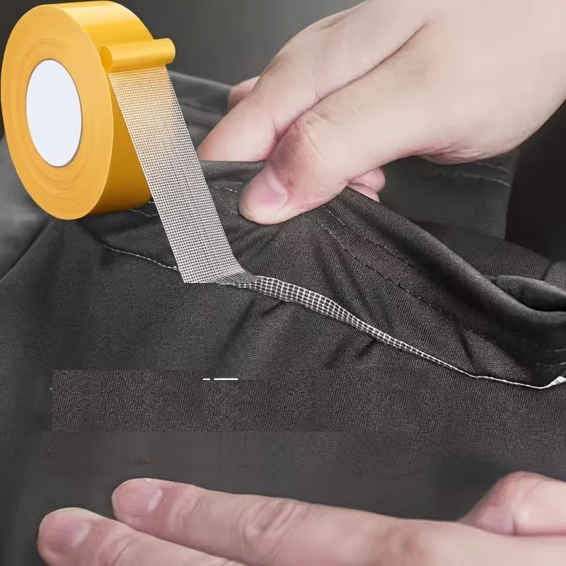 A hand is applying yellow no-sew hem tape to a dark fabric for quick folds or repairs.