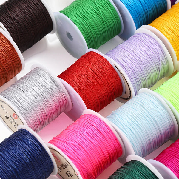 A collection of spools of brightly colored nylon macrame cord for jewelry making arranged in a row.