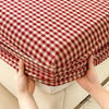 A close-up of a red and cream checkered pure cotton fitted sheet being held by two hands.