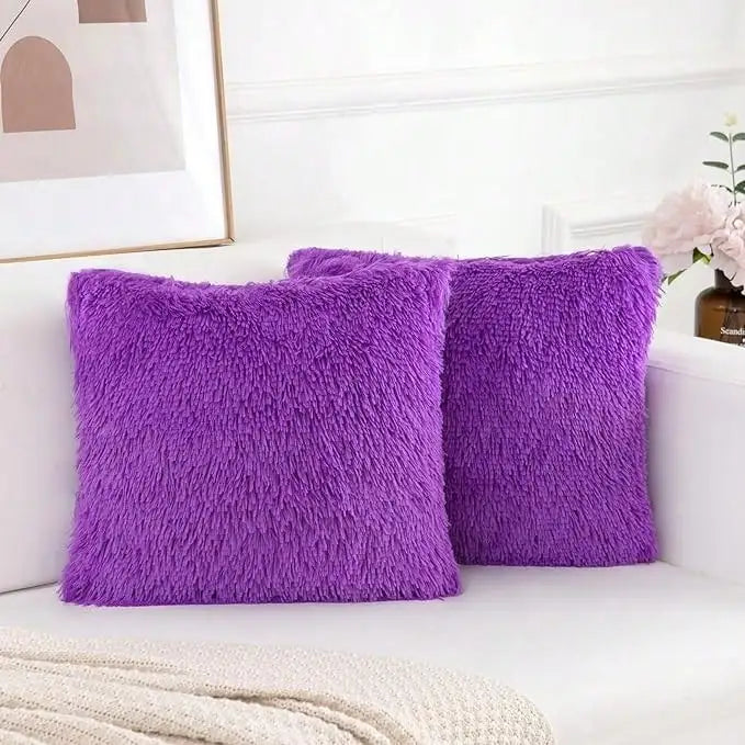 A set of two vibrant purple faux fur throw pillows resting on a white sofa.
