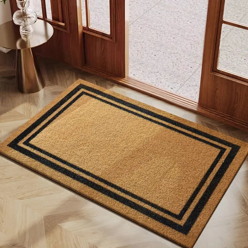 A rectangular natural coconut fiber doormat with black geometric borders placed on a light wooden floor.