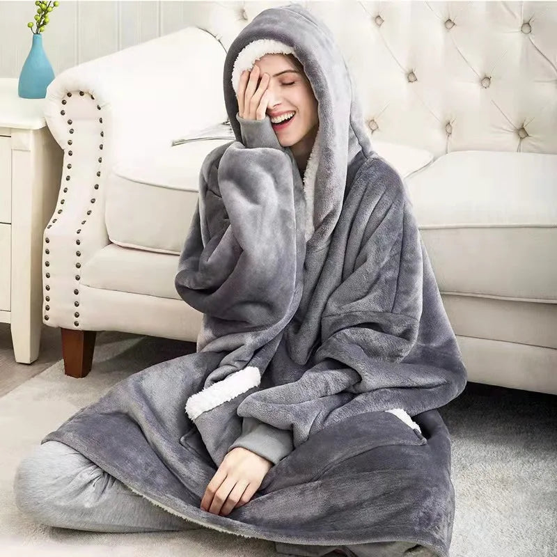 A woman wearing a gray oversized flannel blanket pyjama set is relaxing on a sofa.