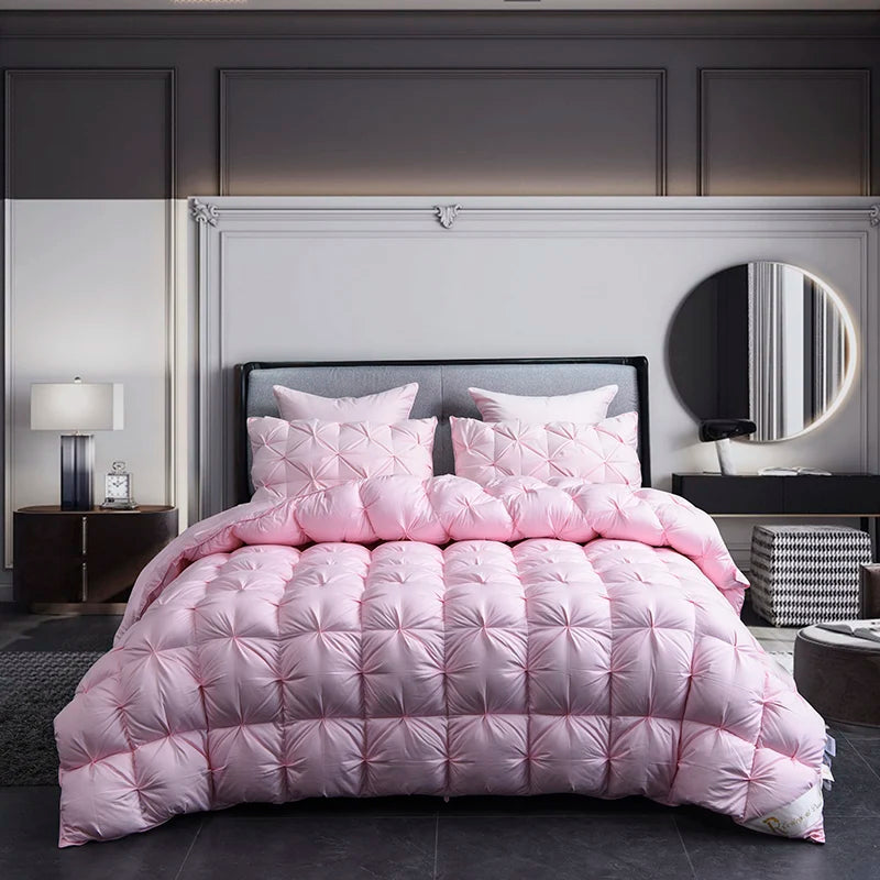 A pink luxury goose down duvet blanket displayed on a bed with a gray upholstered headboard and dark bedding.
