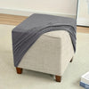 A gray jacquard stretch ottoman slipcover draped over a light beige upholstered ottoman.