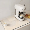 A white electric kitchen drain mat is placed on a light-colored countertop next to a white cup.