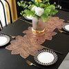 A black table set featuring gold and white tableware, a decorative copper leaf placemat, and a vase of white flowers.