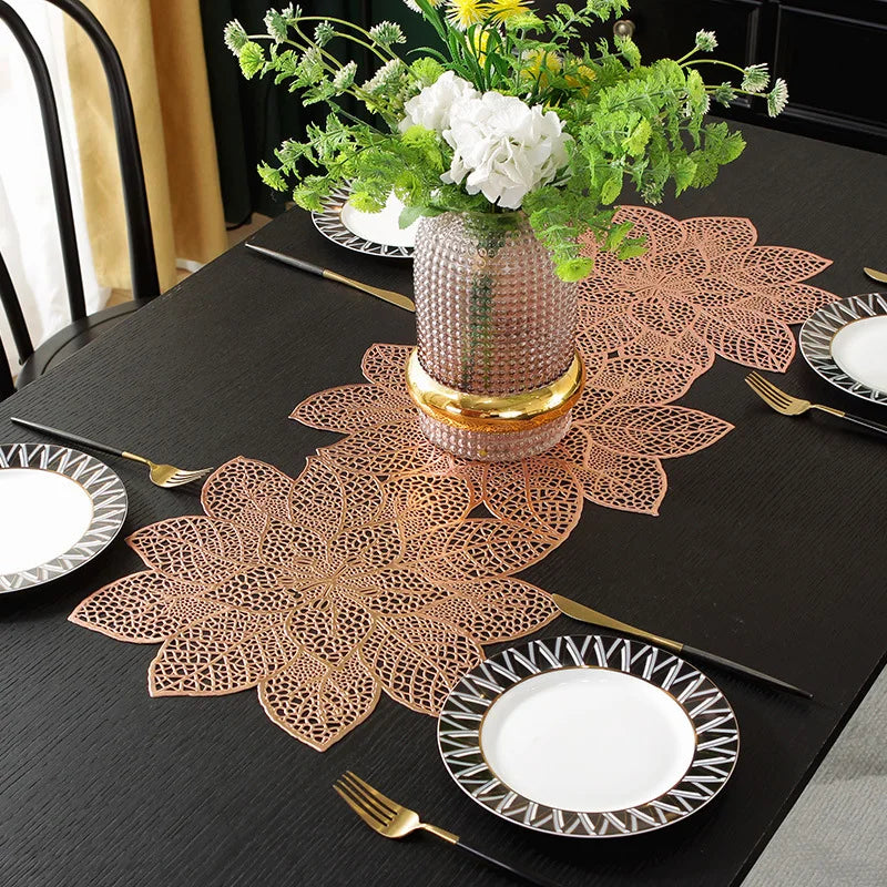 A black table set featuring gold and white tableware, a decorative copper leaf placemat, and a vase of white flowers.
