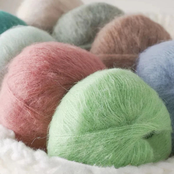 A pile of various colored premium mohair yarn balls, including pink, green, and gray, resting on white fabric.