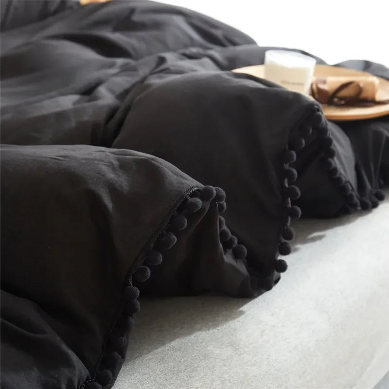 Black soft washed duvet cover set with pom-pom decoration folded on a light surface.