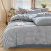 A bed dressed with a blue and white gingham plaid duvet cover and matching pillows, next to a window.