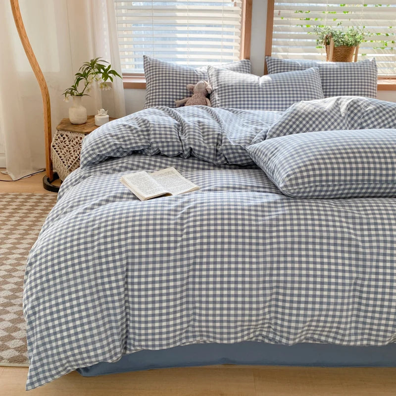 A bed dressed with a blue and white gingham plaid duvet cover and matching pillows, next to a window.