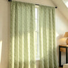 A pair of light green floral print curtains hanging in a window with natural light filtering through.