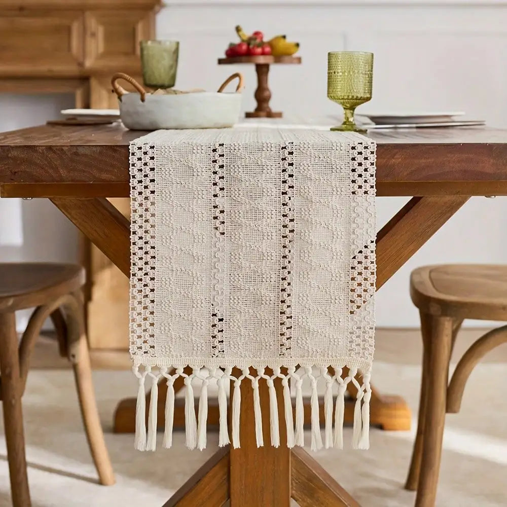 A cream-colored macrame table runner with fringe is displayed on a wooden dining table.