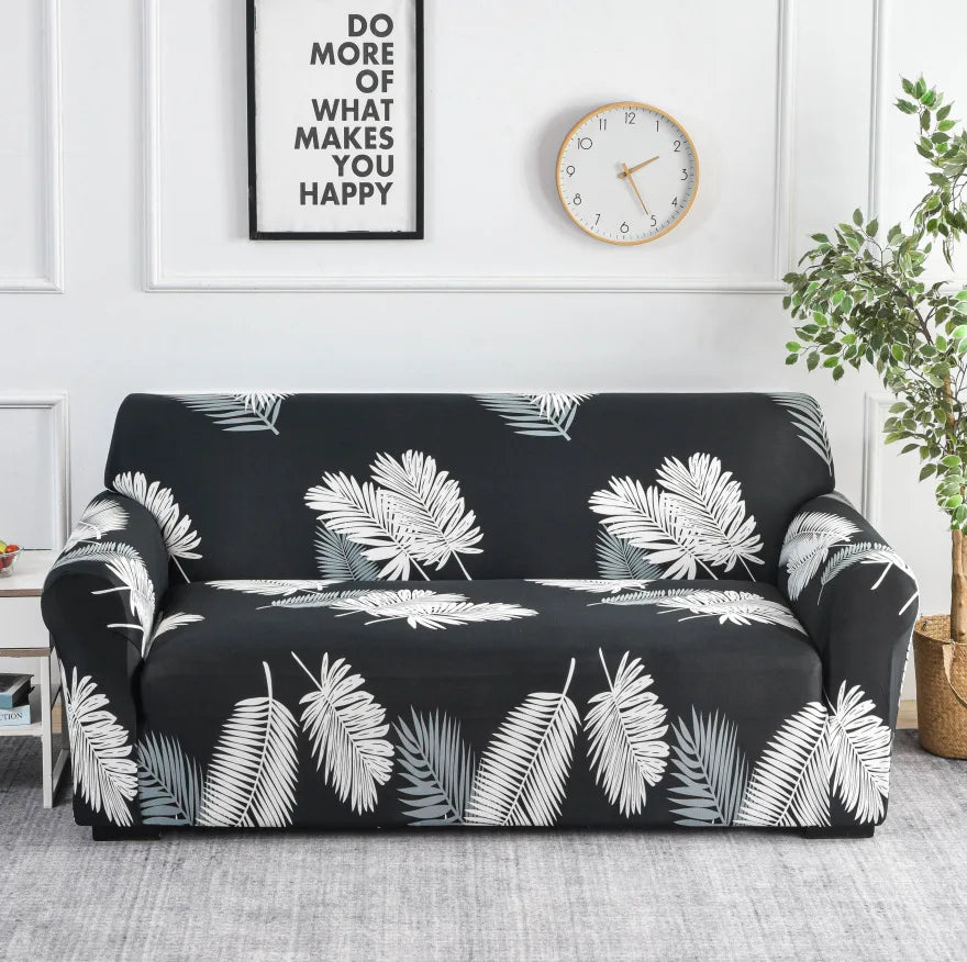 A black sofa covered with a white and teal leaf print elastic protector on a light gray floor.