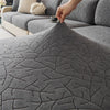 A close-up of a gray jacquard sofa cover featuring an intricate branch pattern, being held by a hand.
