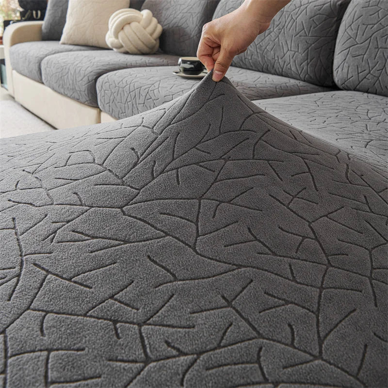 A close-up of a gray jacquard sofa cover featuring an intricate branch pattern, being held by a hand.