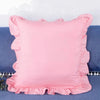 A square pink ruffled pillow cover displayed on a blue fabric background.
