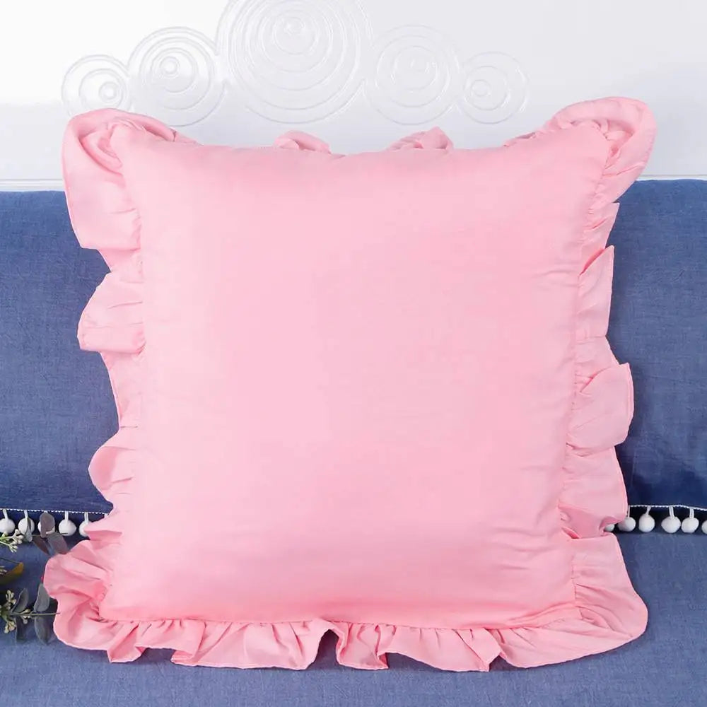 A square pink ruffled pillow cover displayed on a blue fabric background.