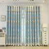 Light blue floral curtains with gold trim hanging in a room.