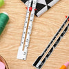 A precision metal sliding sewing gauge and measuring ruler are shown on a wooden surface next to a spool of green thread.