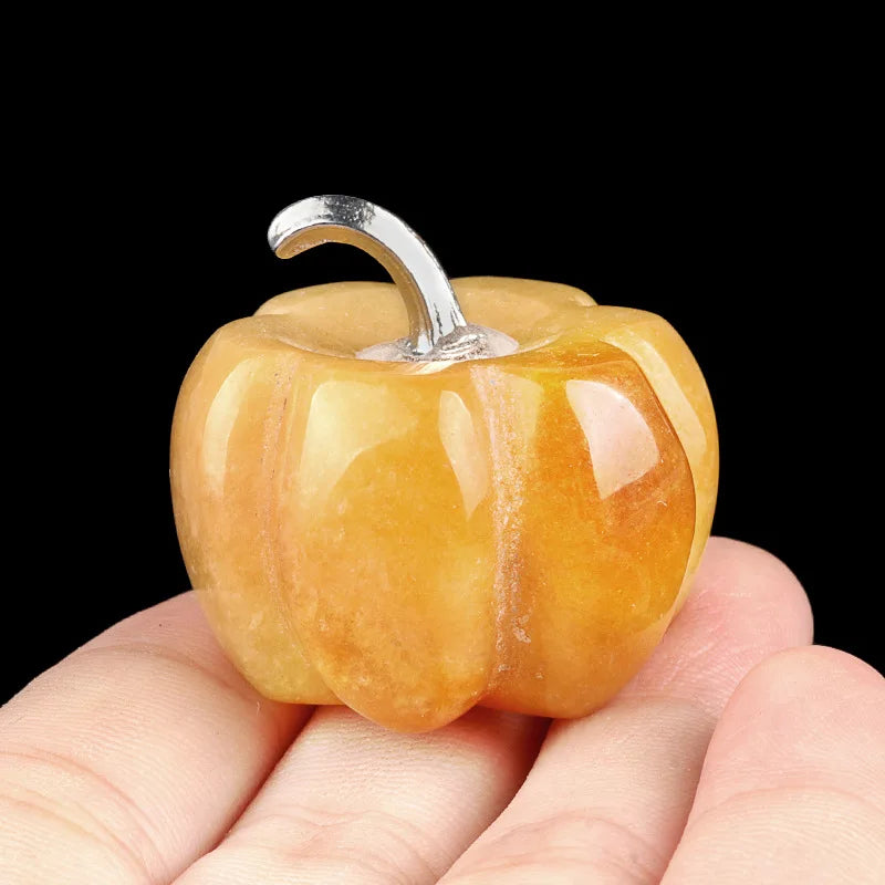 A handcrafted natural stone pumpkin figurine with a silver stem is held in a person's hand.