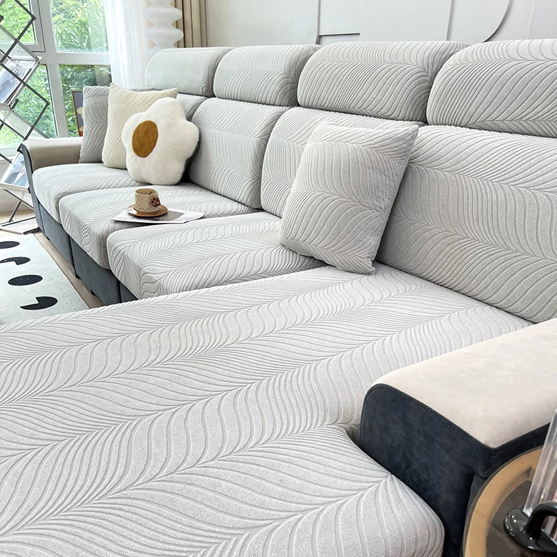 A light gray jacquard stretch sofa cover featuring a wavy texture and cream accent pillows on a modern sofa.