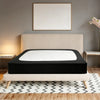 A black box spring protector cover is displayed on a bed with a light beige headboard and white bedding.