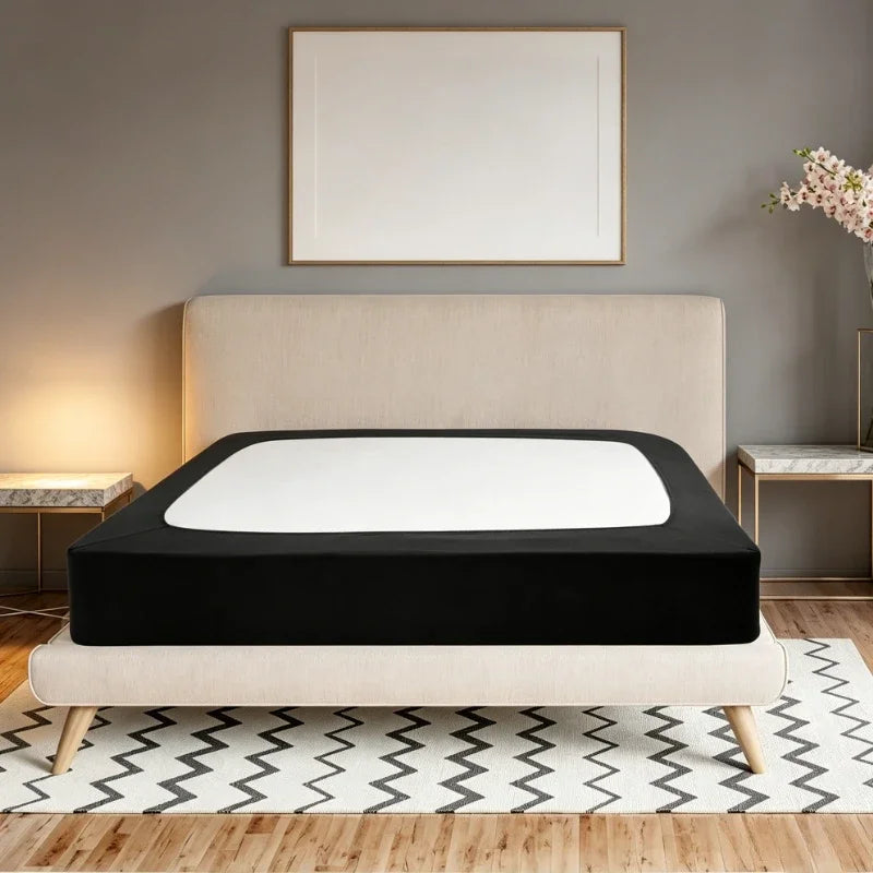 A black box spring protector cover is displayed on a bed with a light beige headboard and white bedding.