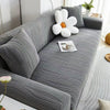 A gray stretchable anti-slip sofa cover is shown in a living room setting with white decorative elements.