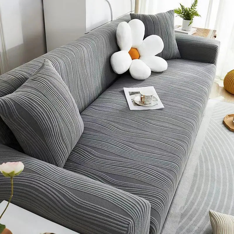 A gray stretchable anti-slip sofa cover is shown in a living room setting with white decorative elements.