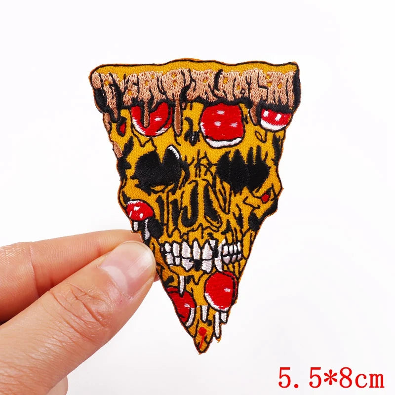 A hand holds a yellow and black embroidery patch depicting a skull face with red accents.