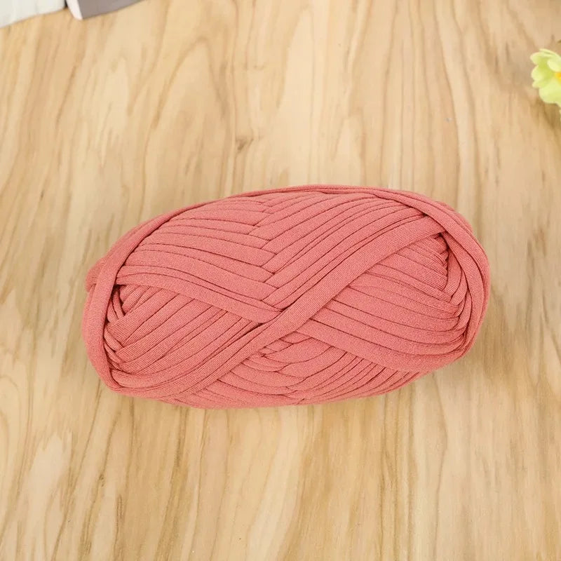 A ball of pink flat thread yarn for crafting and sewing lying on a light wooden surface.